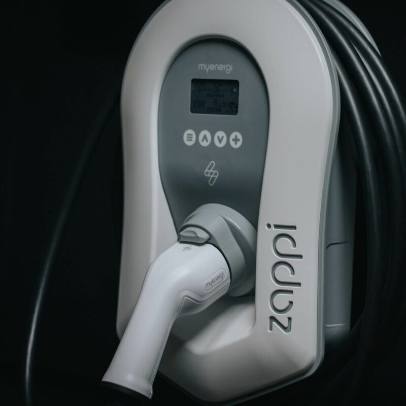 A close-up of a white myenergi zappi EV wall charger with its tethered cable and plug holstered