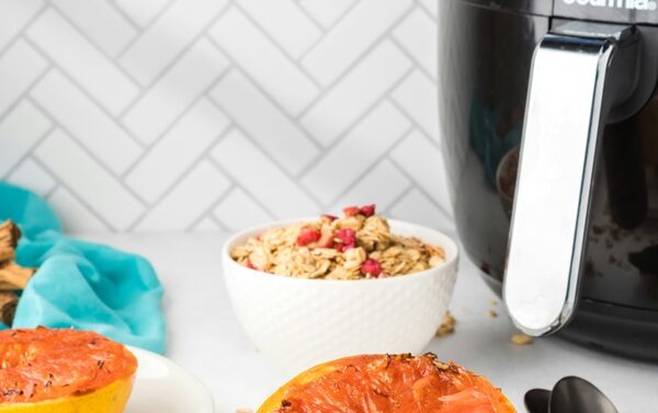 A Gourmia air fryer on a kitchen counter beside bowls of granola and broiled grapefruit breakfasts