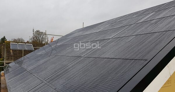 A roof covered in dark in-roof solar panels on a house, with a neighbouring roof and solar thermal panels in the background