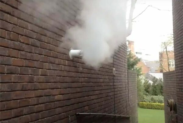 A white boiler flue emitting plumes of steam from a dark brick external wall of a house