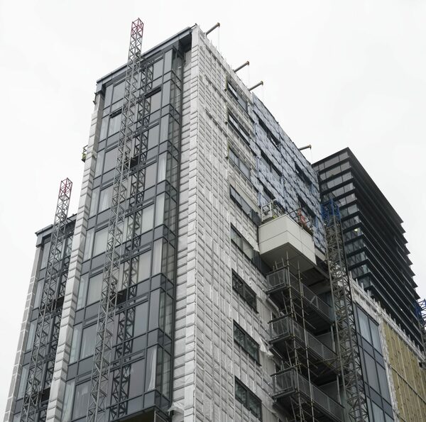 A high-rise apartment block wrapped in scaffolding and protective sheeting while external wall insulation or cladding work is carried out on its facade