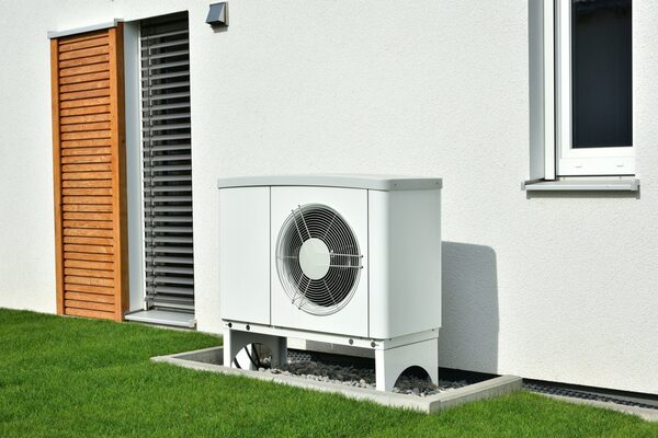 An air source heat pump unit installed on gravel beside the exterior wall of a house with a lawn