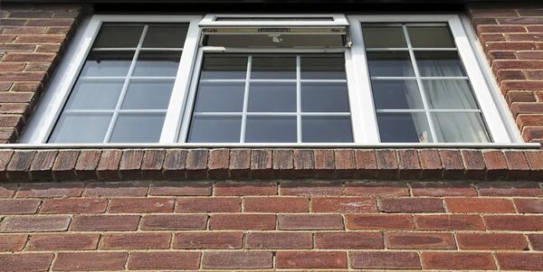 White uPVC double-glazed casement windows with one open top-hung pane, set in a red brick house wall
