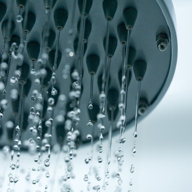 A close-up of a shower head with water dripping from its nozzles