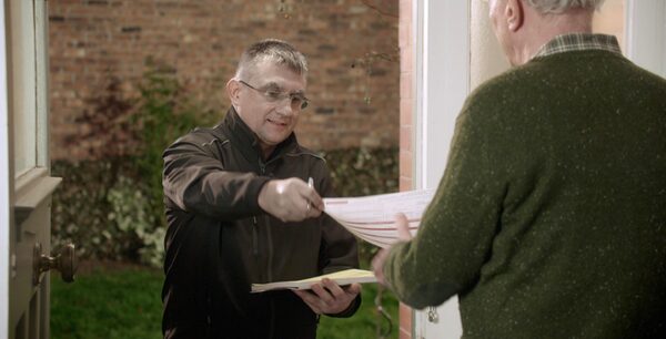 A tradesperson handing paperwork to a homeowner at a front doorway