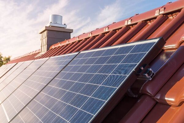 Solar panels mounted on a red-tiled house roof beside a chimney