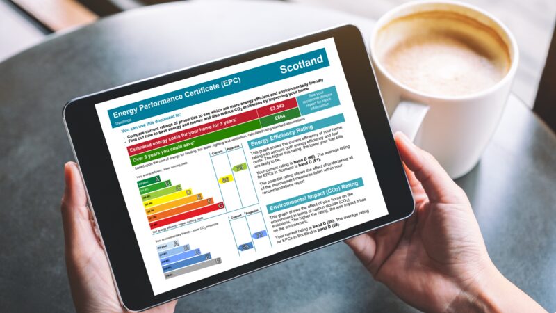 A person holding a tablet displaying a Scottish Energy Performance Certificate (EPC) document next to a cup of coffee