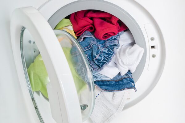 A front-loading washing machine with its door open, full of colourful laundry including jeans and t-shirts