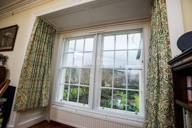 A sash window with secondary glazing fitted in a period living room with floral curtains and a radiator below