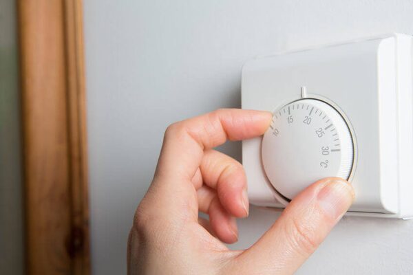 A hand turning the dial of a white wall-mounted mechanical room thermostat