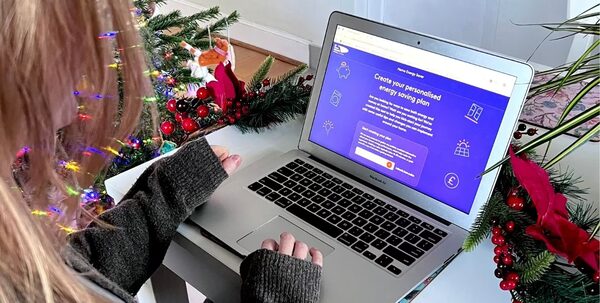 A woman using a laptop displaying a 'Create your personalised energy saving plan' webpage, surrounded by Christmas decorations