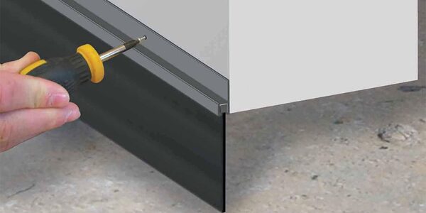 A hand using a screwdriver to fit a black brush draught excluder strip to the bottom of a white door