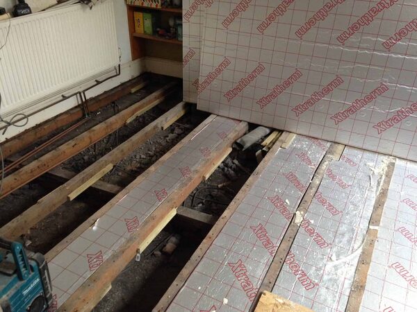 Xtratherm foil-backed insulation boards laid between exposed timber floor joists in a room with the floorboards removed