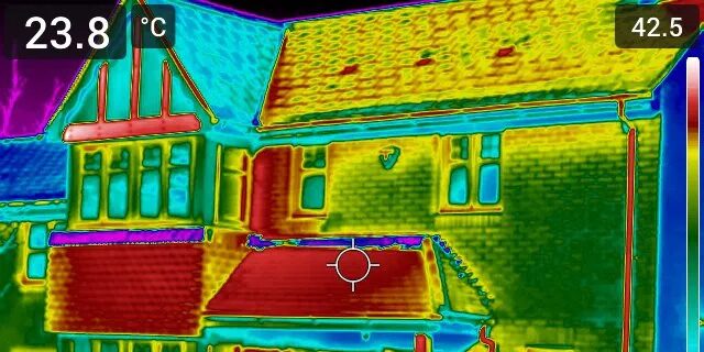 Thermal camera image of a house exterior showing heat loss, with a warm red roof and cooler blue-green walls