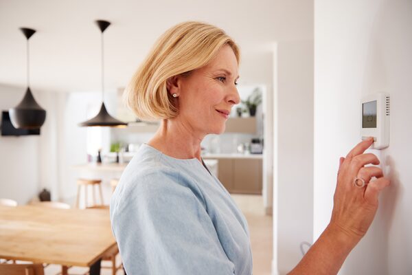 A woman adjusting a wall-mounted digital thermostat in a bright modern home