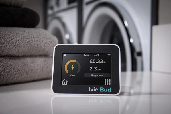 An ivie Bud in-home energy display showing live electricity cost and usage, sitting on a counter in front of a washing machine