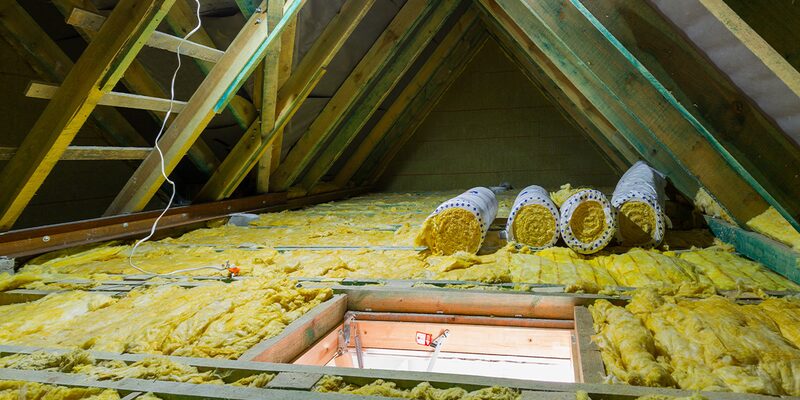 Rolls of yellow glass-fibre insulation laid between joists in a loft with an open hatch