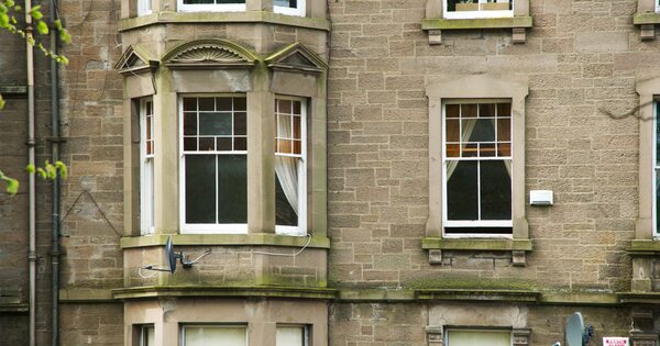 The stone facade of a traditional Scottish tenement building with sash and case windows, including a bay window