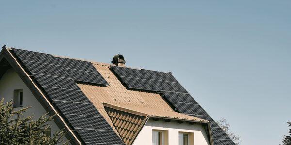 A house roof fitted with black solar panels on tiled slopes under a clear sky
