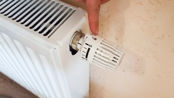 A hand turning the thermostatic radiator valve dial on a white panel radiator