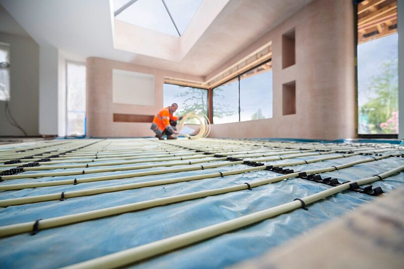 A worker in a high-visibility vest installing underfloor heating pipes across a floor in a room under renovation