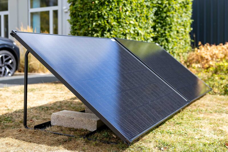 Two ground-mounted solar panels on a metal frame propped with a concrete block in a garden