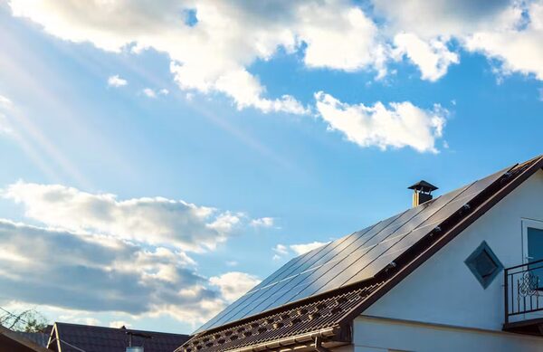 Solar panels installed on the tiled roof of a house under a bright blue sky with clouds