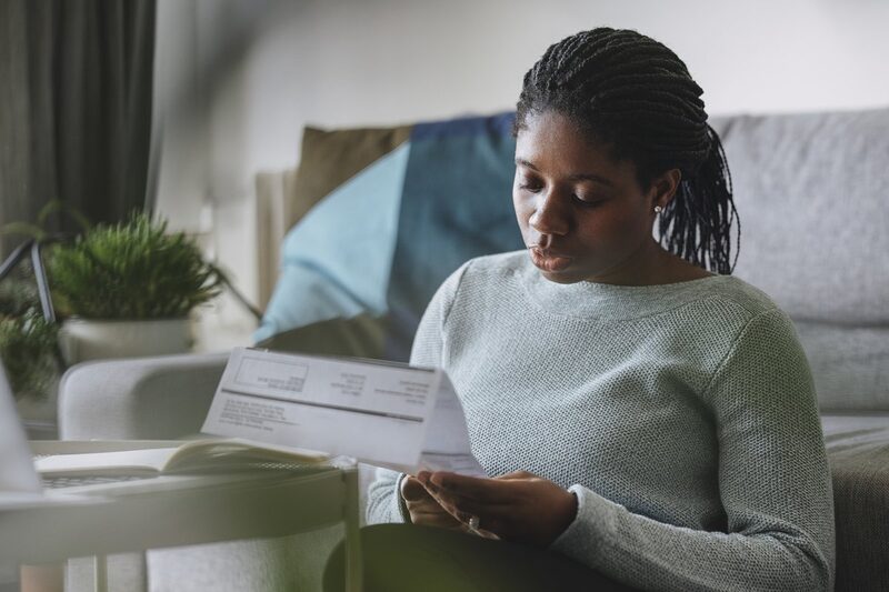 A woman sitting on a sofa at home reading an energy bill letter