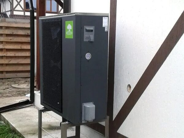 A Mycond air source heat pump unit installed outside a house on a metal stand against a white wall