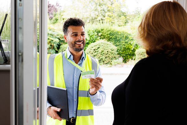 An energy assessor in a hi-vis vest showing his ID badge to a householder at her front door