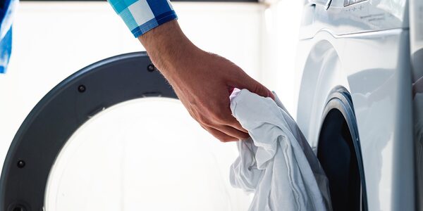 A person loading white laundry into the drum of a front-loading washer dryer