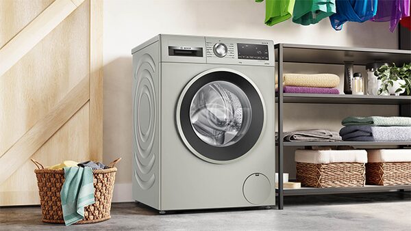 A Bosch washing machine in a utility room with shelving, towels and a laundry basket