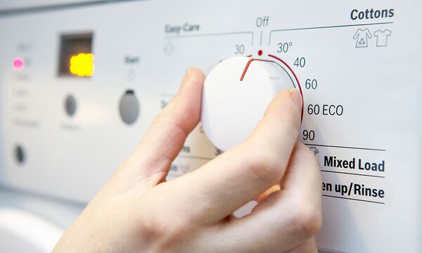 A hand turning the programme dial of a washing machine to the 30 degree cottons setting