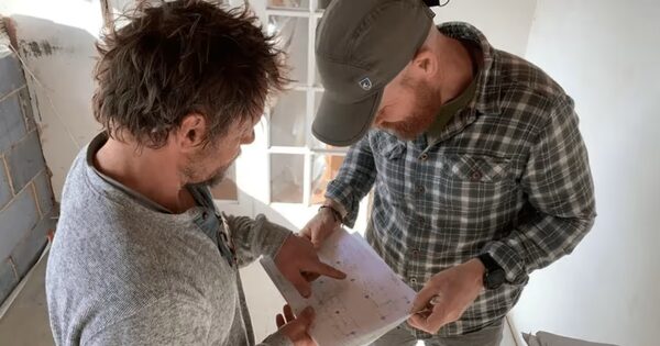 Two men reviewing a printed document together in a room undergoing retrofit works