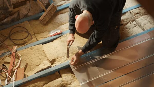 A workman kneeling in a loft installing reflective foil insulation between joists over mineral wool insulation