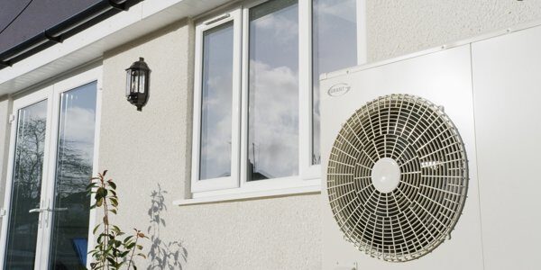A Grant air source heat pump installed on the exterior wall of a house beside a window and lantern light