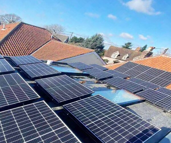 A large array of solar panels installed on a tiled residential rooftop with neighbouring houses in the background