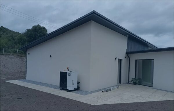 A heat pump unit installed outside a modern white-rendered house on a paved patio