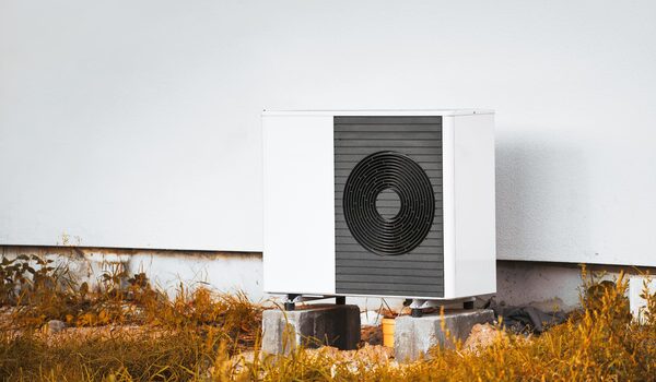 An air source heat pump outdoor unit mounted on concrete blocks against a white wall