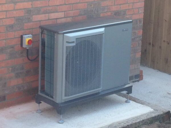 An air source heat pump unit installed outside a brick house wall on a concrete base