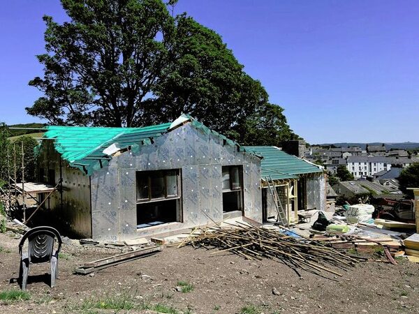 A house under renovation wrapped in foil-faced insulation board with a green tarpaulin roof, on a building site