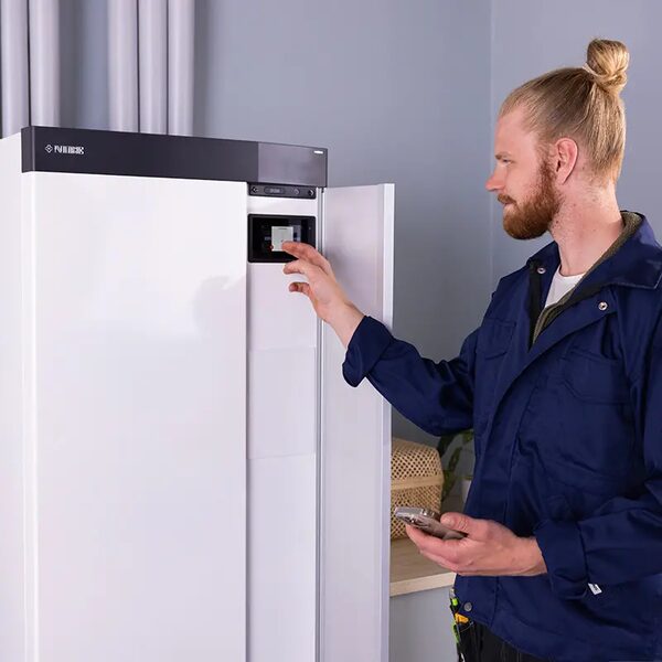 A technician in a blue work jacket adjusting the control panel of a white NIBE indoor heat pump or boiler unit installed in a home