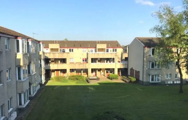 A block of 1960s-style social housing flats seen across a grassy courtyard on a sunny day
