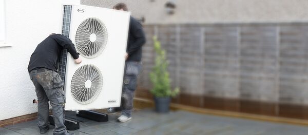 Two installers positioning a large Grant air source heat pump unit outside a house