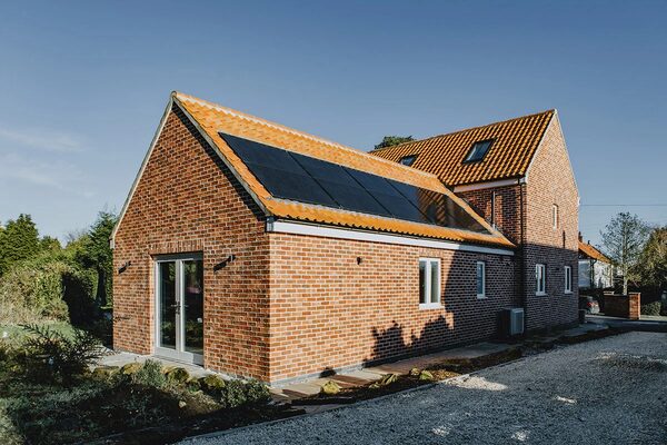 A modern brick eco-home with solar panels on its tiled roof and a heat pump unit at the side of the house