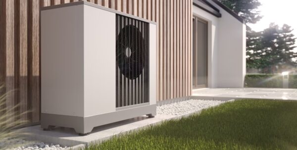 An air source heat pump unit installed outside a modern house on a gravel bed beside a lawn