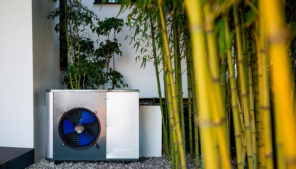 An Ecoforest air source heat pump unit installed outside a house, partly hidden by bamboo plants