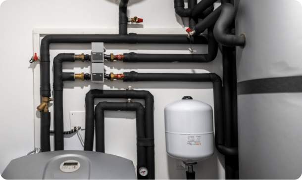 An installed heat pump system with insulated pipework, valves, an expansion vessel and a hot water cylinder in a plant room