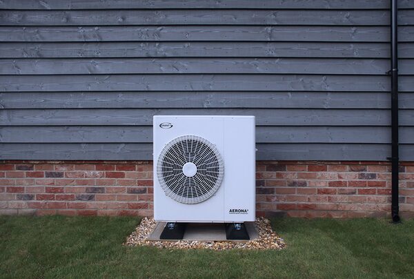 A Grant UK Aerona air source heat pump installed outside a house against a grey weatherboard and brick wall