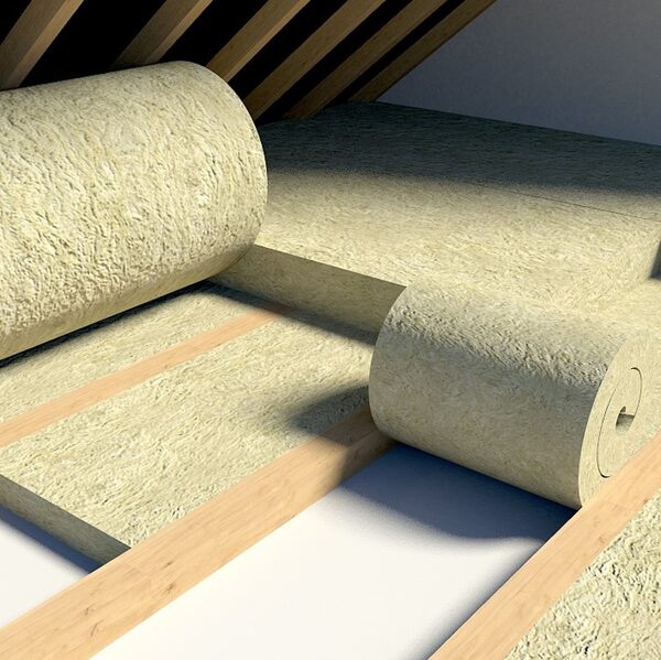 Rolls of mineral wool loft insulation being laid between wooden joists in a loft